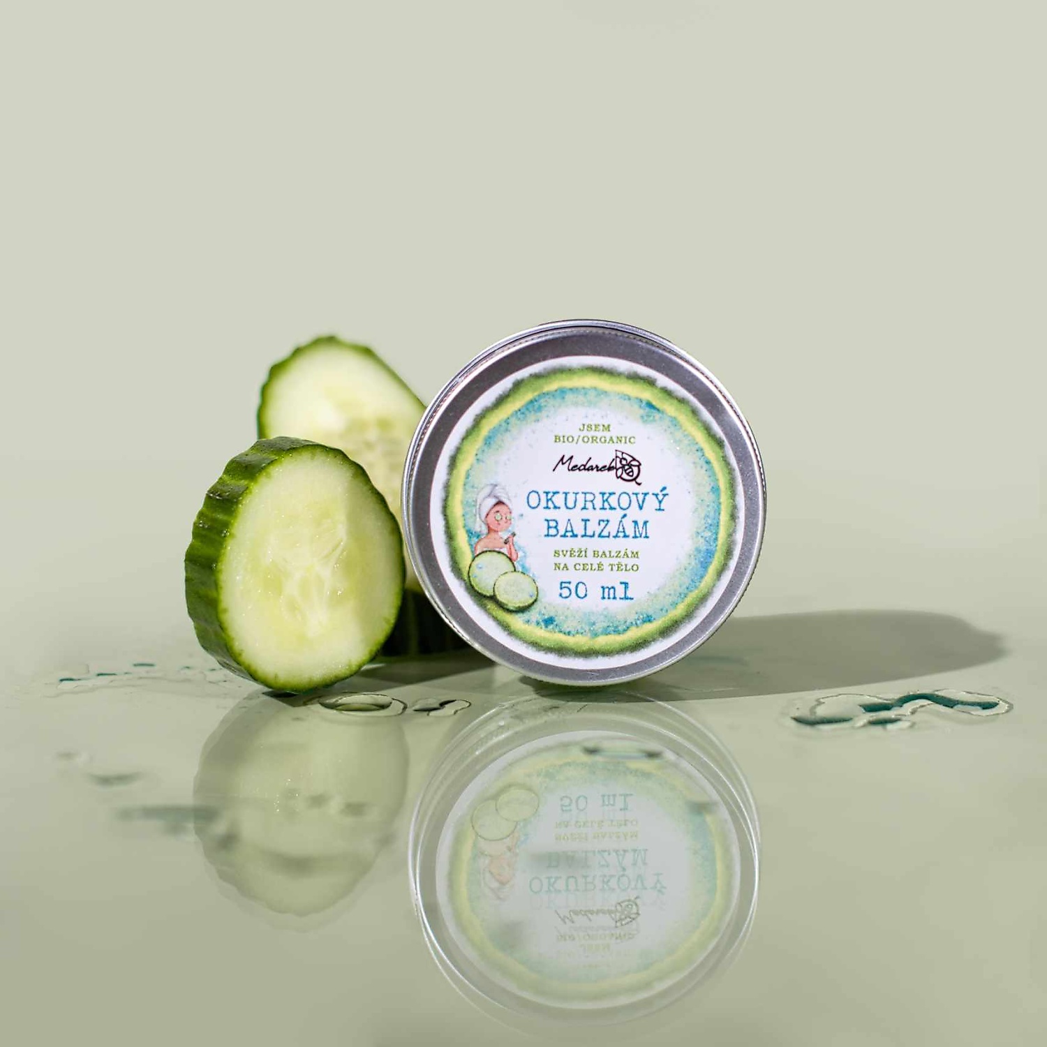Medarek Cucumber Balm (50 ml) tin with fresh cucumber slices and water droplets on a glossy green surface.